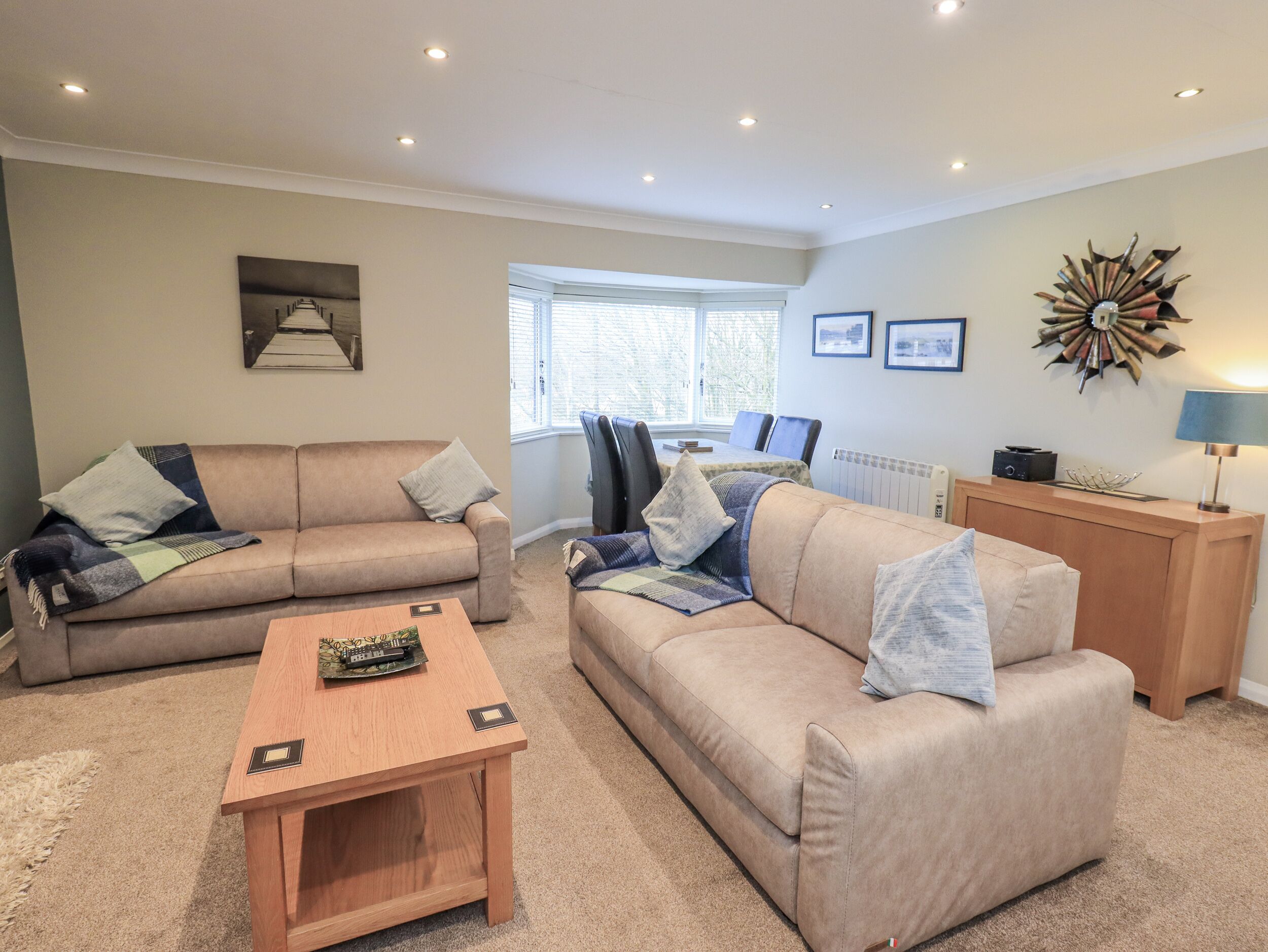 A living room with two sofas, a coffee table, a dining table with chairs, a radiator, and a decorative wall piece.