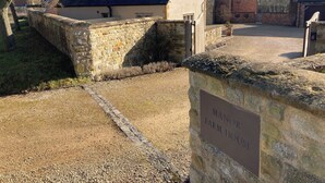 Un mur de pierre sur lequel est apposée une plaque indiquant : « MAISON DE LA FERME DU MANOIR ».