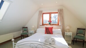 Une chambre à coucher avec un lit blanc, deux tables de chevet, une fenêtre avec des rideaux et une vue sur les arbres.