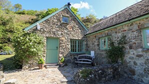 Une petite maison en pierre avec une porte verte, un banc et des plantes en pot dans la cour.