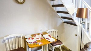 Un coin repas avec une table dressée pour deux personnes, des chaises blanches avec des coussins marron, une table en bois et une lampe.