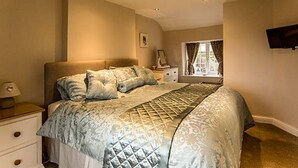 Une chambre à coucher avec un grand lit, une table de chevet, une commode, une fenêtre avec des rideaux et un téléviseur fixé au mur.