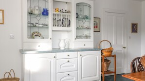 Una cocina con armarios blancos, encimera azul y comedor con mesa y sillas de madera.