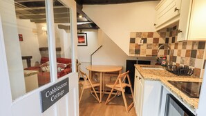 A compact kitchen with a wooden table and chairs, a tiled backsplash, and a sign indicating a cottage-style accommodation. - Cobblestone Cottage (Ambleside)