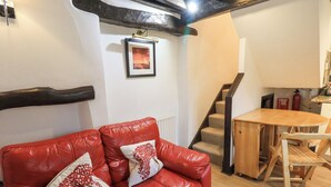A red leather sofa with decorative pillows, a wooden dining table, and a staircase leading to an upper floor. - Cobblestone Cottage (Ambleside)