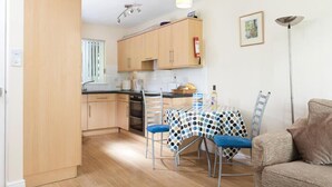 Una cocina compacta con armarios de madera, una mesa de comedor con mantel de lunares y un sofá en la sala.