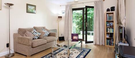 A living room with a beige sofa, a glass coffee table, a bookshelf, and a large window with curtains.