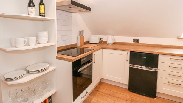 A modern kitchen with white cabinetry, a black dishwasher, and a wooden countertop. - Fairfield Cottage (Lincoln)
