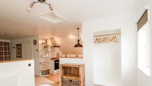 A bedroom with a large bed, a wooden chest, and a kitchen area with a hanging light fixture. - Fairfield Cottage (Lincoln)