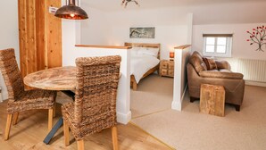A cozy room with a wooden dining table, wicker chairs, a bed with a wooden headboard, a brown sofa, and a small wooden stool. - Fairfield Cottage (Lincoln)