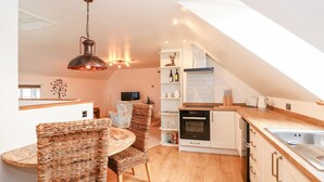 A modern kitchen with a wooden countertop, white cabinets, and a built-in oven. There is a dining area with wicker chairs and a table. - Fairfield Cottage (Lincoln)
