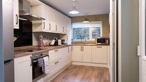 A modern kitchen with white cabinetry, a wooden countertop, a built-in oven, and a microwave. - Noble Cottage (Keswick)