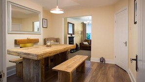 A dining area with a wooden table and benches, a hanging light fixture, and a mirror on the wall. - Noble Cottage (Keswick)