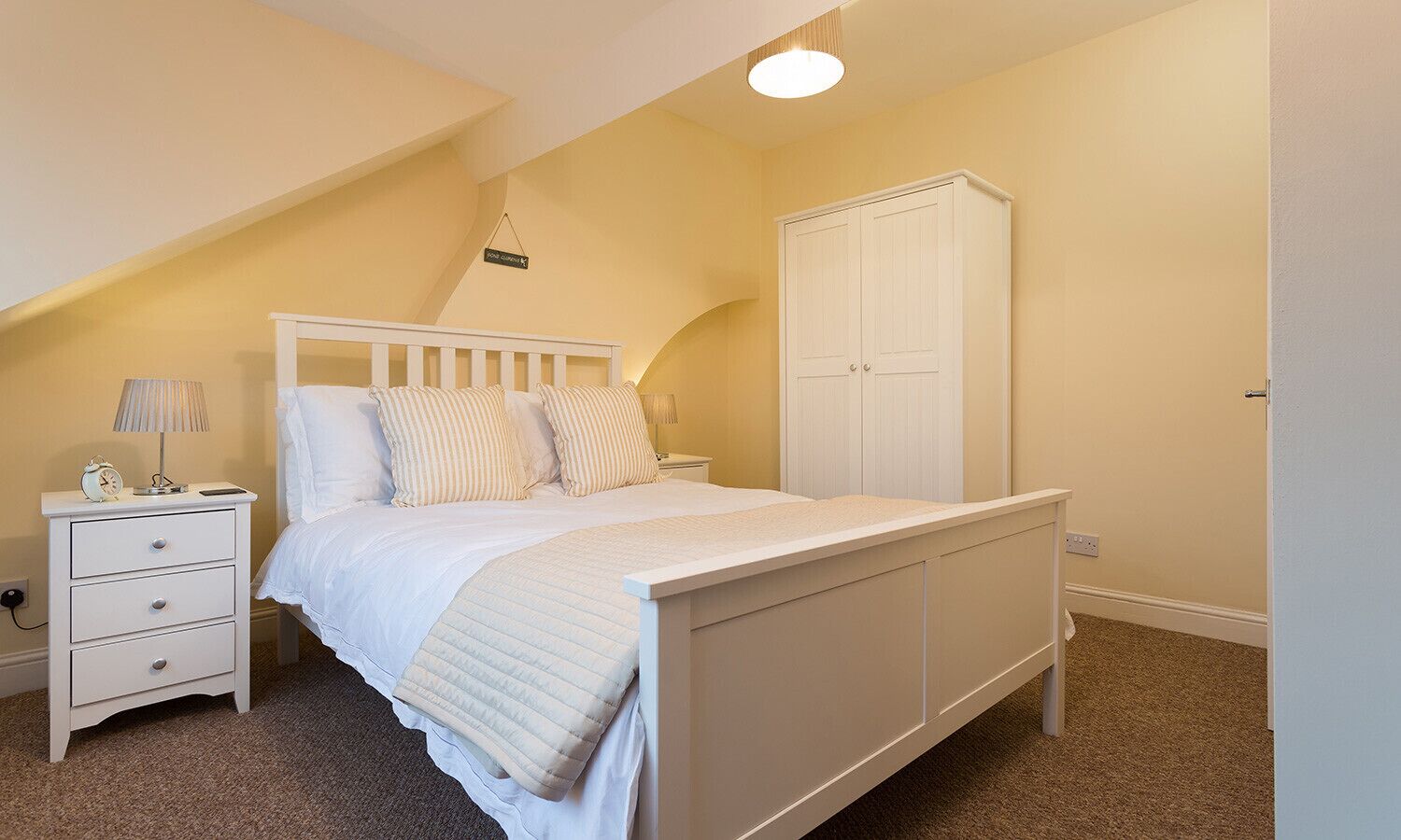 A bedroom with a bed, a nightstand, a lamp, and a wardrobe.