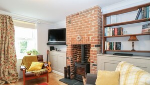 A cozy living room with a brick fireplace, a bookshelf, a television, and a comfortable seating area. - 21 Florence Road (Lowestoft)