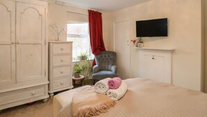 A bedroom with a bed, a chair, a wardrobe, a television, and a window with red curtains. - 21 Florence Road (Lowestoft)