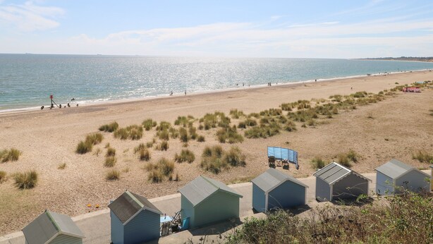 A beach with several small, light-colored beach huts and a sandy beach with sparse grass. - 21 Florence Road (Lowestoft)