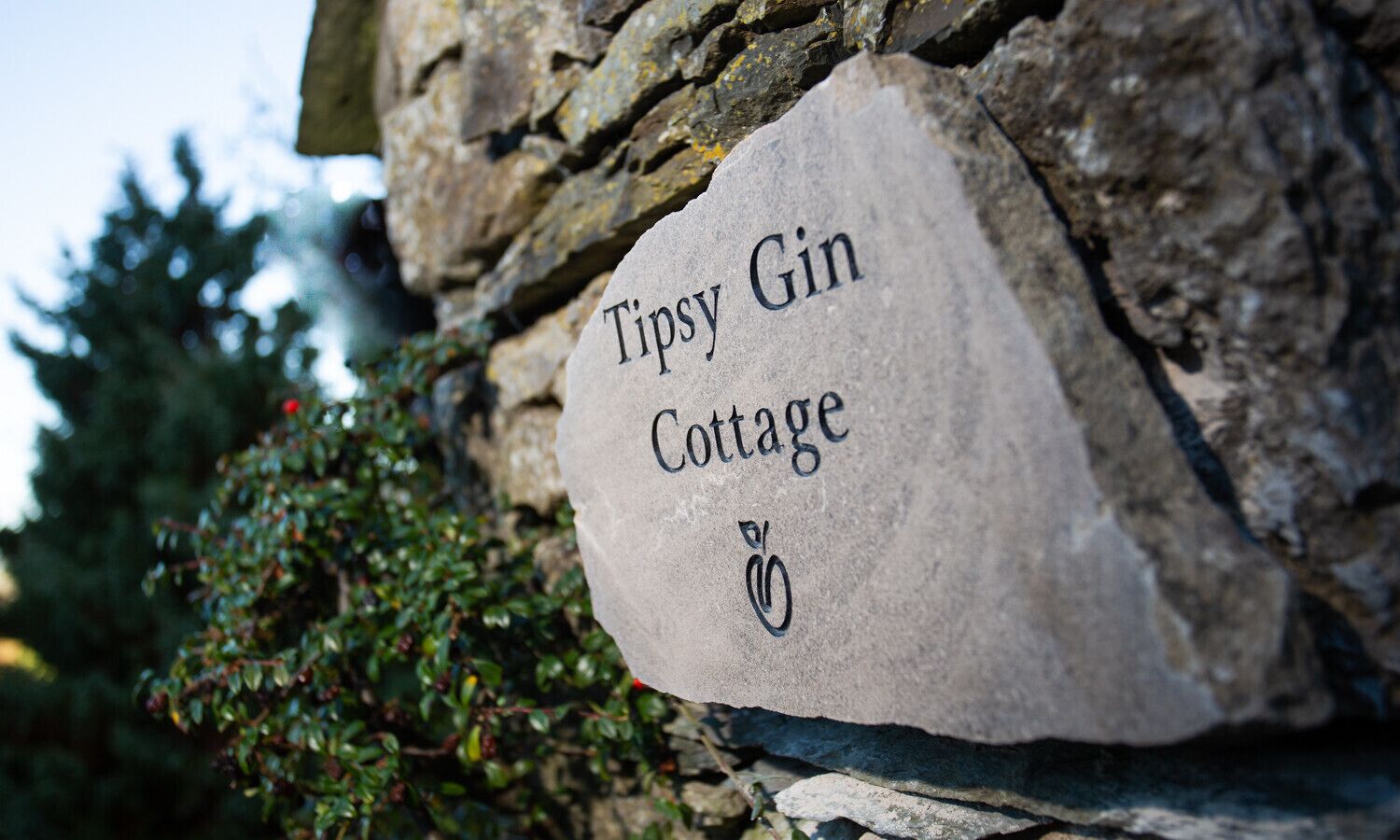 A stone sign with the text "Tipsy Gin Cottage" and a small logo.