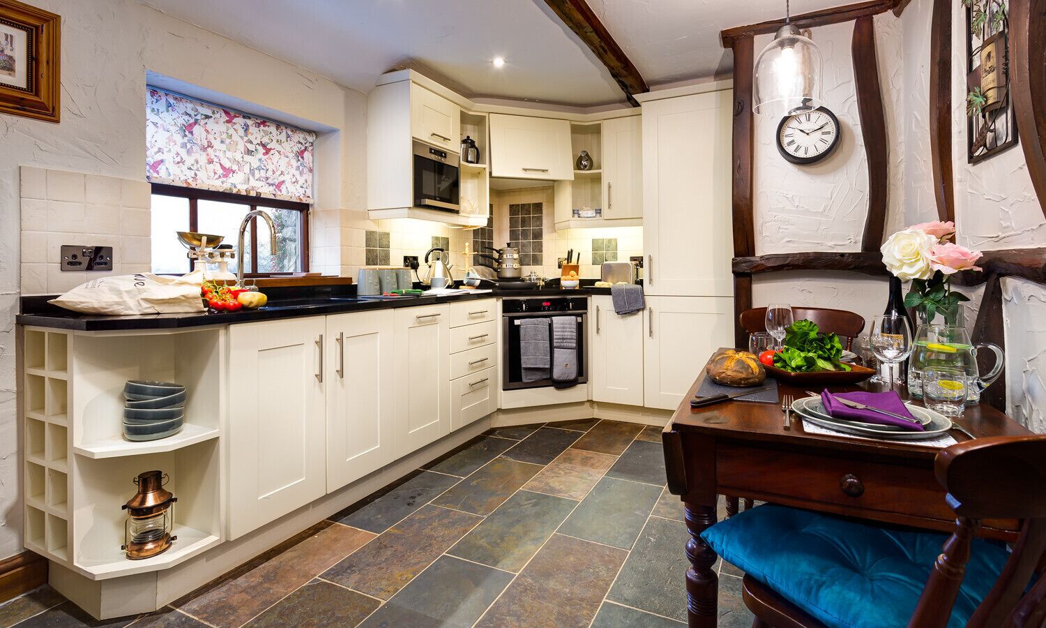 A kitchen with white cabinets, a black countertop, and a dining table set with plates, glasses, and a vase of flowers.