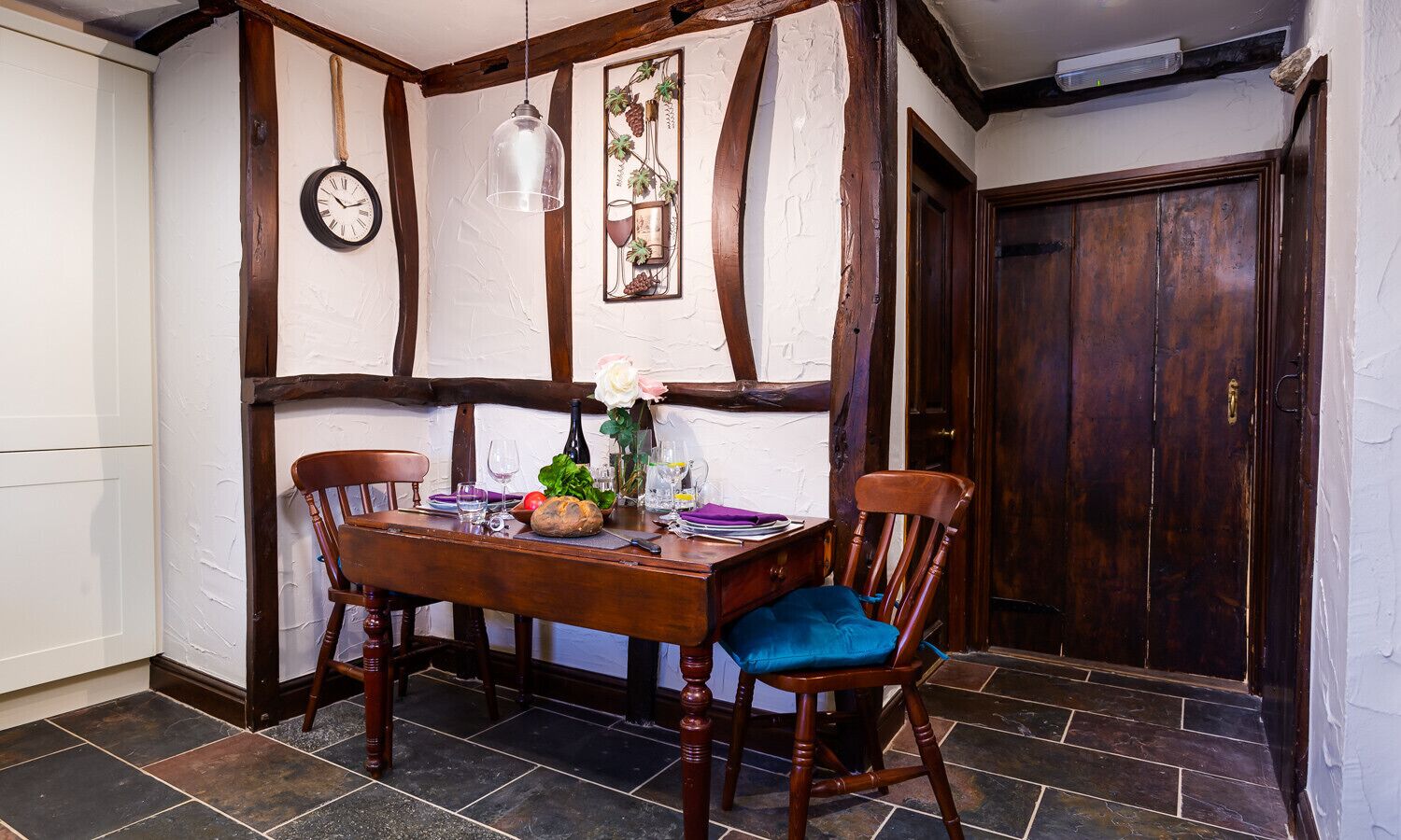 A dining area with a wooden table, two chairs, a clock, and a decorative wall panel.