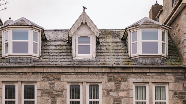 A building with a stone facade, multiple windows, and a bird perched on the roof. - Kinnaird House (Grantown-on-Spey)