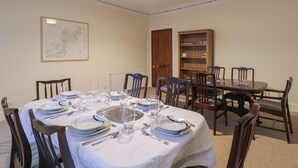 A dining room with a round table set for six, surrounded by wooden chairs. A bookshelf is against the wall to the right. - Kinnaird House (Grantown-on-Spey)