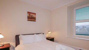 A hotel room with a bed, two bedside tables, a lamp, a painting on the wall, and a window with blinds. - Kinnaird House (Grantown-on-Spey)