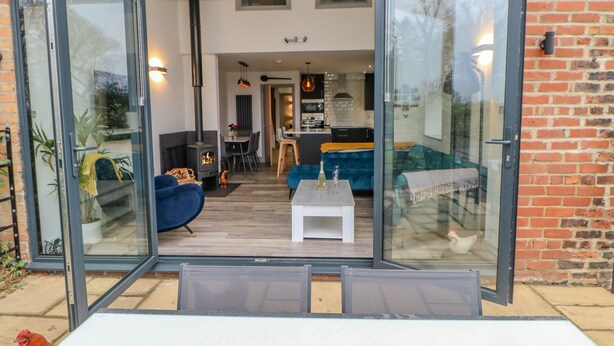 A modern house with a glass door entrance, a cozy living area with a sofa and a coffee table, and a visible kitchen in the background. - The Hay Barn (Houghton le Spring)