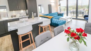 A modern kitchen with a marble island, a blue sofa, and a dining area with a white table and chairs. - The Hay Barn (Houghton le Spring)