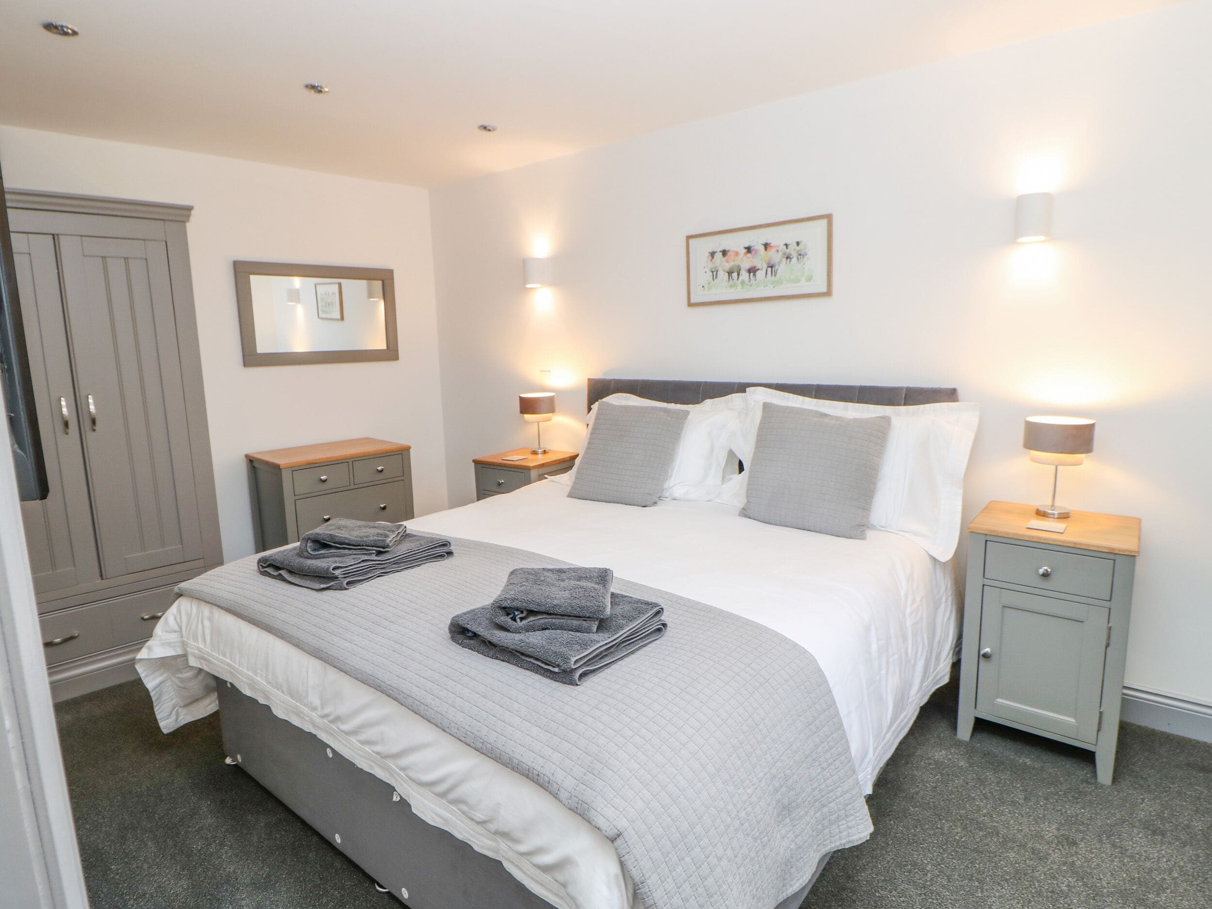 A neatly arranged bedroom with a large bed, two bedside tables with lamps, a wardrobe, and a framed picture on the wall.