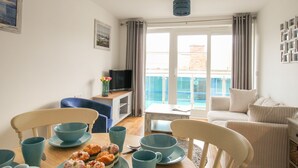 A dining area with a table set for four, a television, and a view of a pool through the glass doors. - Nautical Breeze (Weymouth)
