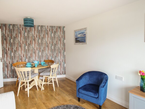 A dining area with a wooden table and chairs, a blue armchair, and a painting on the wall.