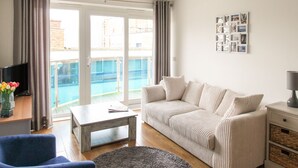 A living room with a sofa, a coffee table, a TV, and a balcony with a pool. - Nautical Breeze (Weymouth)