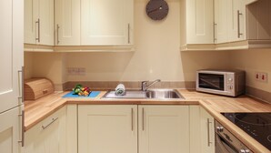 A compact kitchen with light-colored cabinets, a stainless steel sink, a microwave, and a stove. - Nautical Breeze (Weymouth)