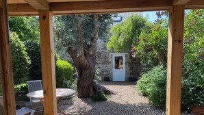 A wooden pergola with a gravel path, a stone wall, and a door leading to a garden area. - Little Brook (Weymouth)