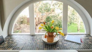 A window with a view of a garden, a vase with flowers, and a notebook on a tiled table. - Little Brook (Weymouth)