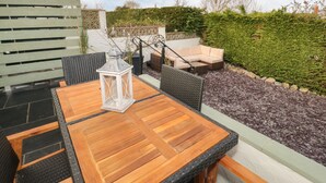 A patio with a wooden table and chairs, a white lantern, and a sofa. - Hardy Cottage (Tyn-y-Gongl)