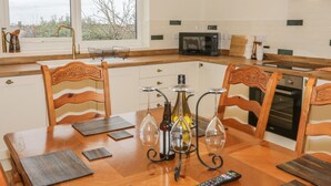 A modern kitchen with white cabinets, a microwave, and a window overlooking a garden. - Hardy Cottage (Tyn-y-Gongl)
