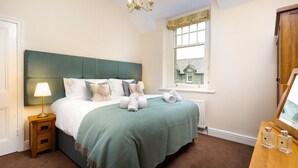 A neatly made bed with a green headboard, a bedside lamp, and a window with a view of a house.