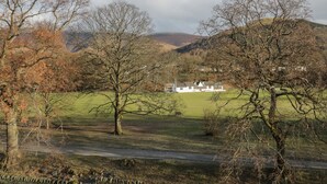 Un paysage rural avec un bâtiment blanc entouré d’arbres et de collines en arrière-plan.