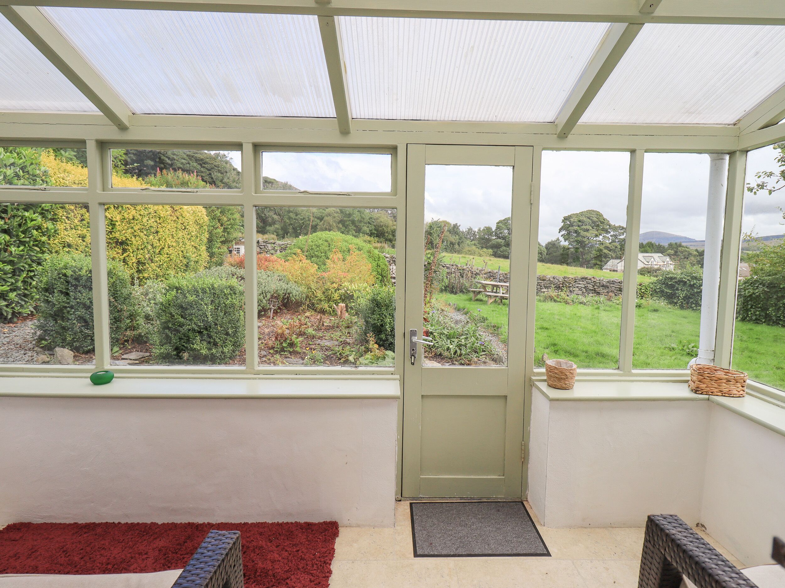 A conservatory with a door, a red rug, and a wicker basket on the windowsill.