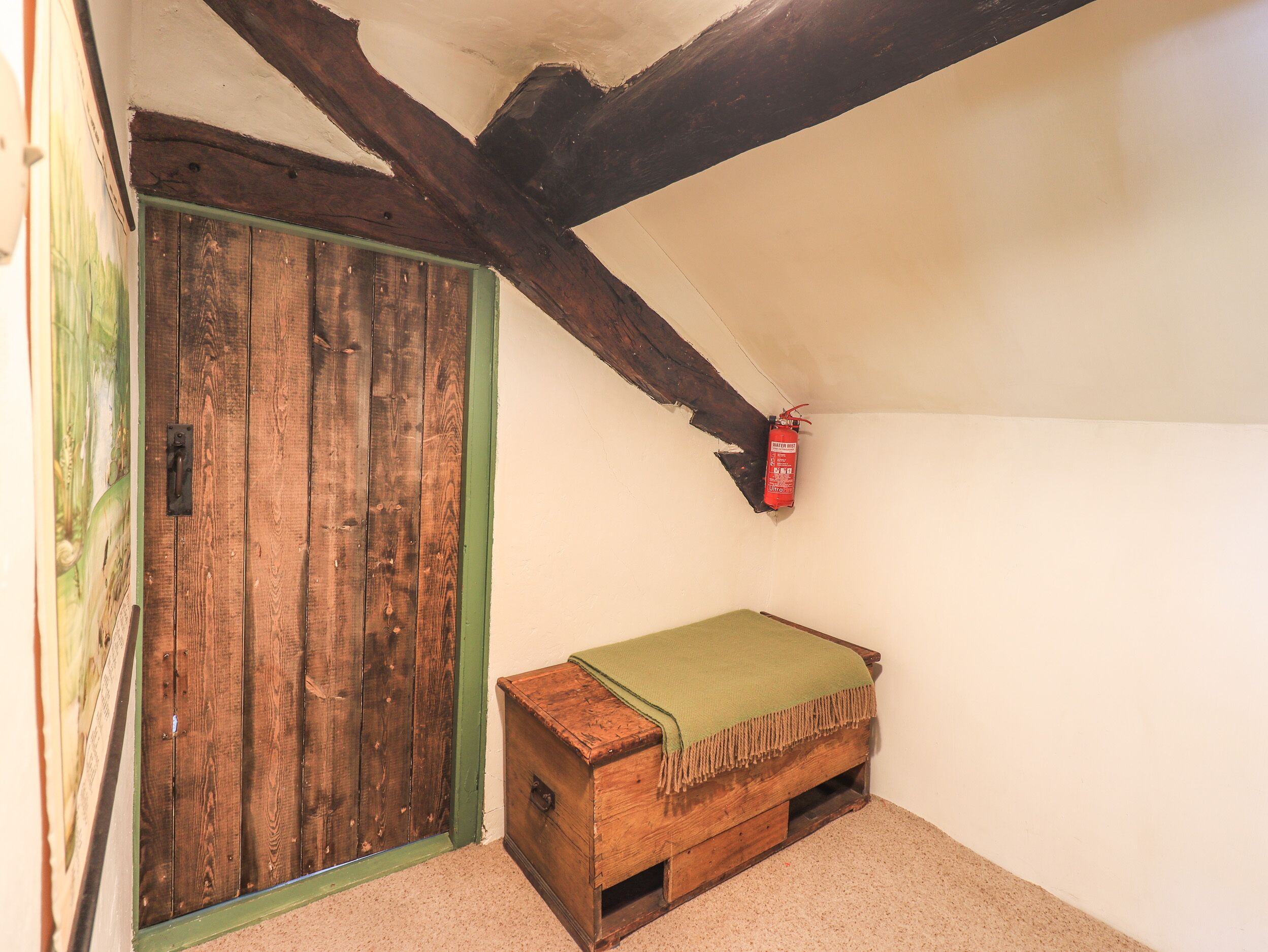 A room with a wooden door, a small wooden chest, and a fire extinguisher on the wall.