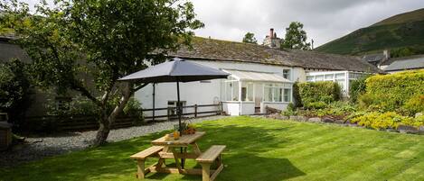 A white house with a conservatory, a wooden picnic table, and a large umbrella.