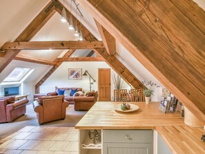 A loft-style living room with exposed wooden beams, a wooden dining table, and a cozy seating area with sofas. - Lady Pond Retreat (Ashbourne)