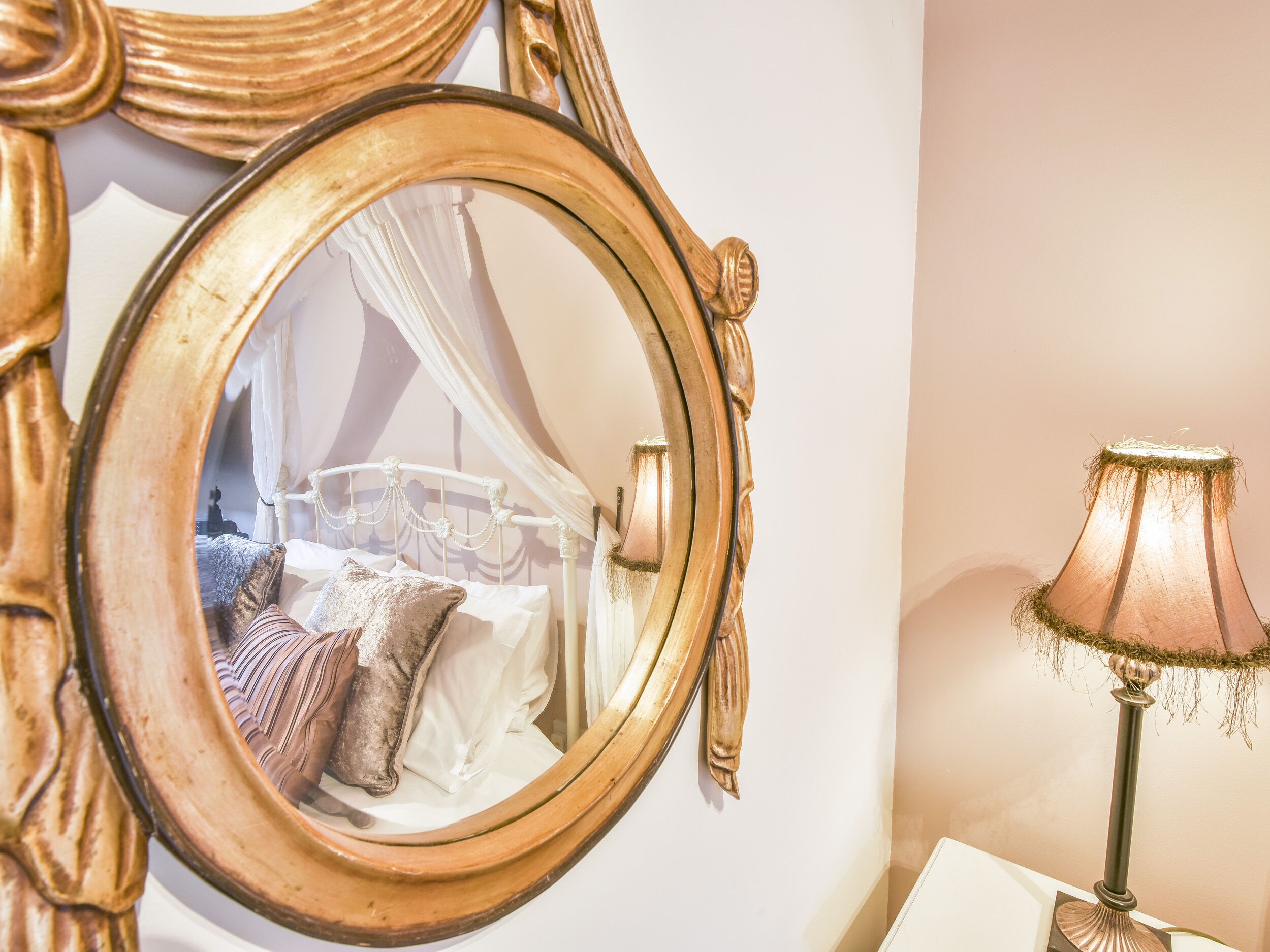 A bedroom with a bed, a bedside lamp, and a mirror reflecting the room.