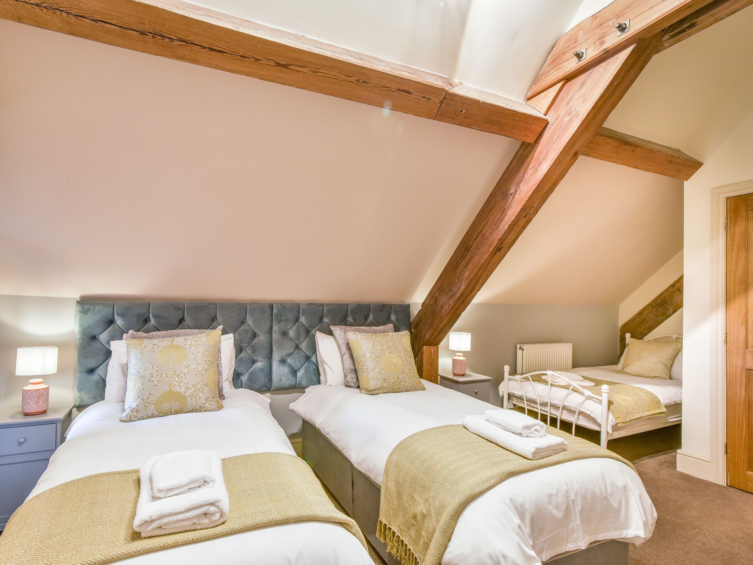 Une chambre avec deux lits, des poutres en bois, un radiateur et des lampes de chevet.