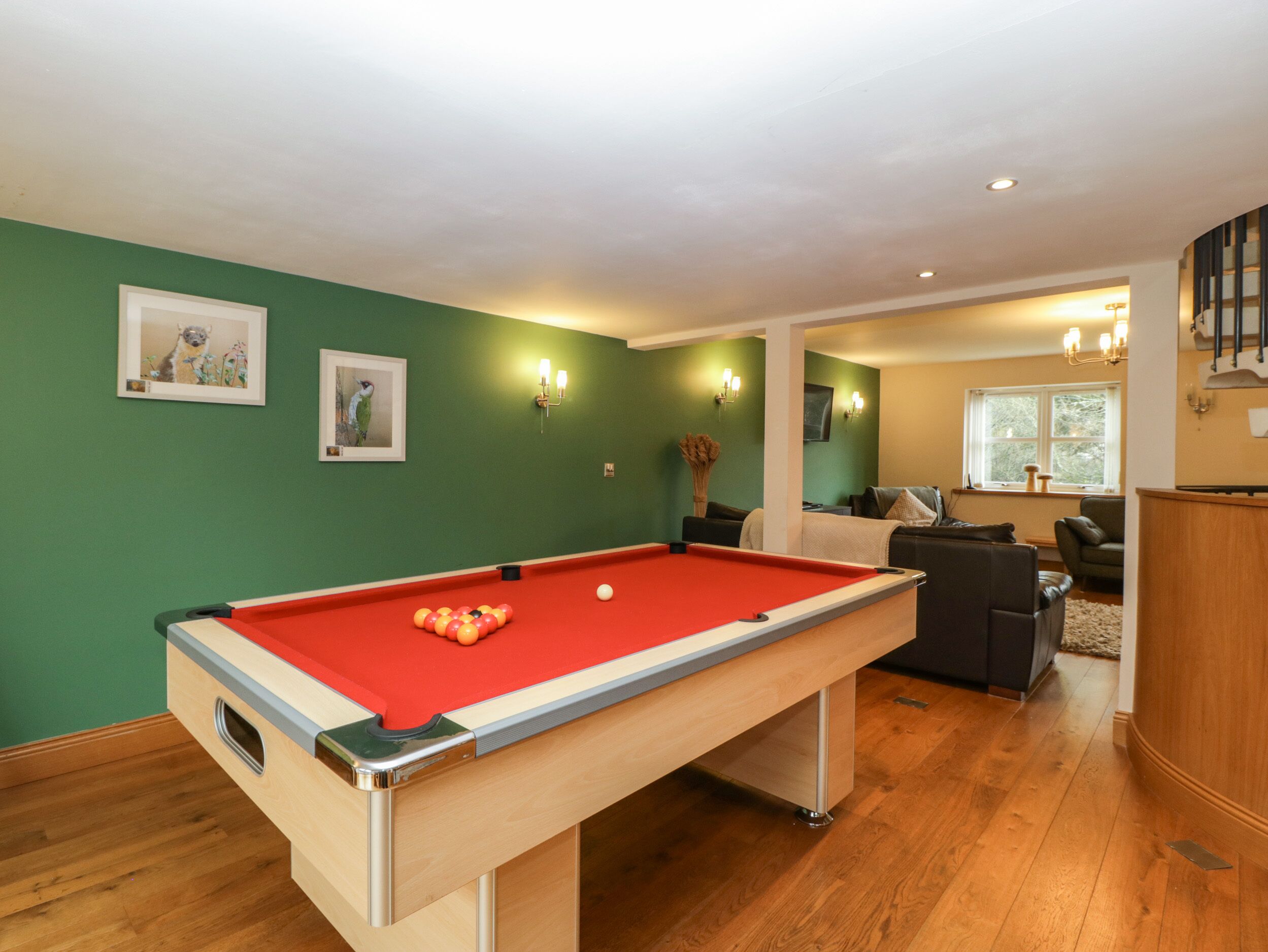 A pool table in a room with green walls, wooden flooring, and a seating area with a sofa and armchairs.