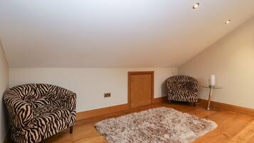 Una habitación con techo alto, piso de madera, dos sillones a rayas de cebra, un tapete mullido, una puerta de madera y una pequeña mesa con un jarrón.