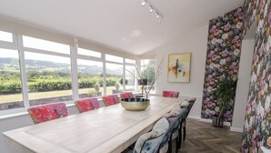 Une salle à manger avec une grande table, des chaises aux couleurs vives et une vue sur la campagne, grâce à de grandes fenêtres.