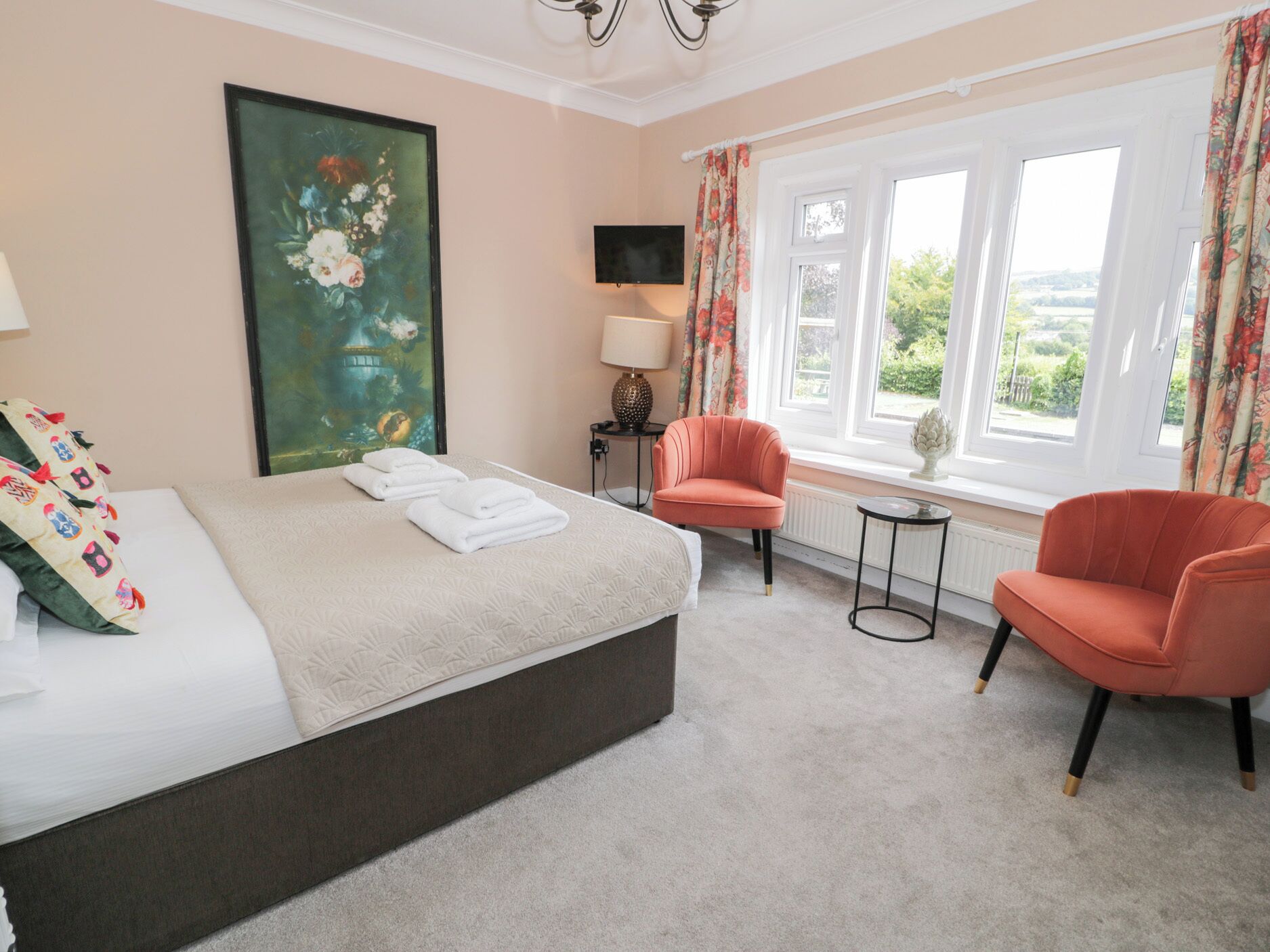 A bedroom with a bed, two chairs, a painting, a TV, and a window with curtains.